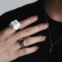 Hand shown against a black background, adorned with a unique keycap ring on the middle finger, characterized by its large, square shape with a prominent white keycap design. The ring finger showcases a creative monster design ring with a jagged, tooth-like pattern,  subtle star-shaped pendant on a silver necklace