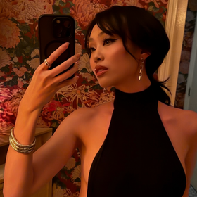 Woman taking a mirror selfie wearing a black dress with floral wallpaper in the background